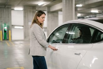 Femme en blazer gris évaluant une voiture électrique blanche en stationnement urbain pour un leasing en 2026