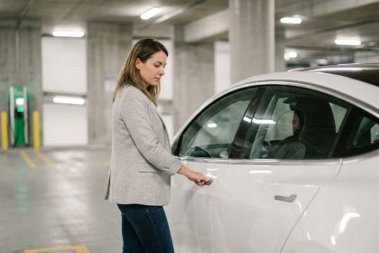 Femme en blazer gris évaluant une voiture électrique blanche en stationnement urbain pour un leasing en 2026
