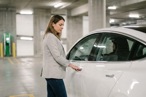 Femme en blazer gris évaluant une voiture électrique blanche en stationnement urbain pour un leasing en 2026